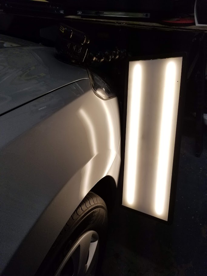 Fender dent visible under PDR light board before repair